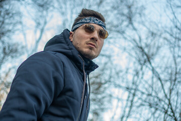 Portrait of a young and stylish man in sunglasses and a bandana. Male model showing fashion. Style concept.