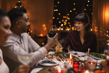 holidays, party and celebration concept - multiethnic group of happy friends having christmas dinner at home and drinking wine