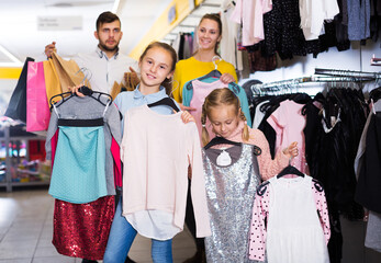 Two small happy sisters with parents satisfied with purchases in children clothing shop