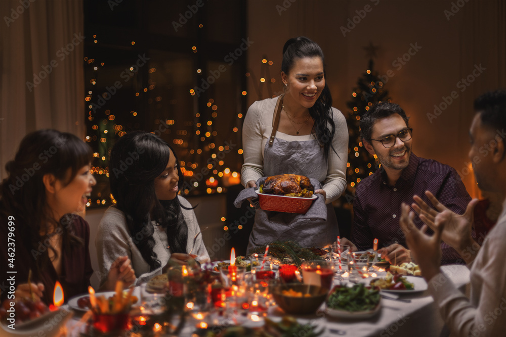 Wall mural holidays and celebration concept - multiethnic group of happy friends having christmas dinner at hom