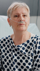 Portrait of retired woman with nasal oxygen tube and oximeter, sitting in bed. Sick patient having...