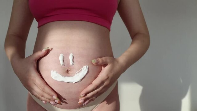 Drawn cute face on the belly of a pregnant woman. Pregnant girl stroking her belly 
