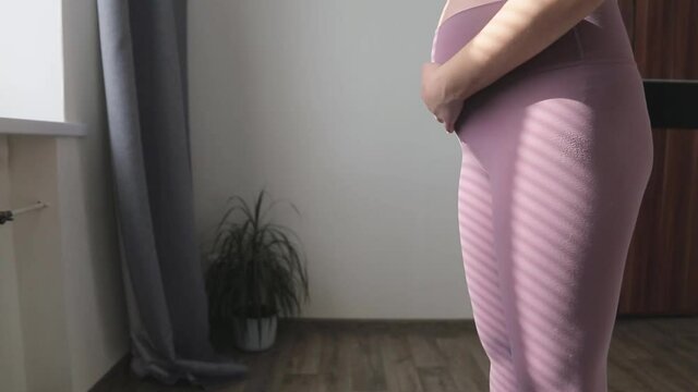 Pregnant woman in sportswear stroking her belly