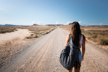 Young caucasian woman with a grey backpack walking in the middle of a dessert at Bardenas, Navarre, Basque Country.