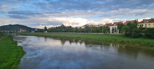 Natural beauty of blue sky and calm water of river in Mukachevo, Ukraine. Beautiful landscape with river and houses at sunset. Scenic view of the old town embankment on a cloudy summer day at dusk.