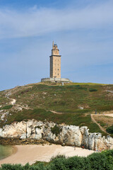 the tower of hercules can be seen at the top of the hill above the cliffs overlooking the beach
