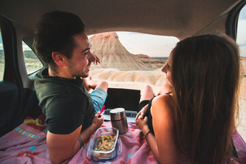 One woman and one man eating and chatting in a car while travelling at Bardenas Reales desert, Navarra, Basque Country.
