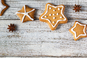 Border of Christmas gingerbreads in the shape of a star with patterns of glaze and spices on a white wooden background.