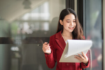 Fototapeta premium Asian young female executive reading a document in her hands while working at the office