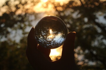 Eine Hand hält eine Glaskugel mit der Reflektion der Sonne und Bäumen im Hintergrund aufgenommen...
