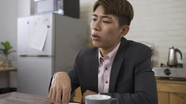 closeup depressed Asian male in business suit is lack of energy while eating bread for breakfast before work in the dining room at home.