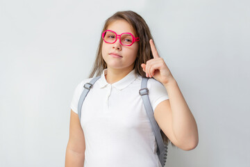 Portrait of little schoolgirl in pink glasses with backpack holding index finger up