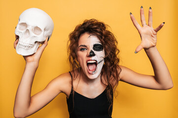 Studio shot of a girl in a costume of evil spirits at a Halloween costume party with a skull in her...