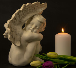 Statue of sad angel with burning candle and flowers as symbol of pain, fear and end of life....