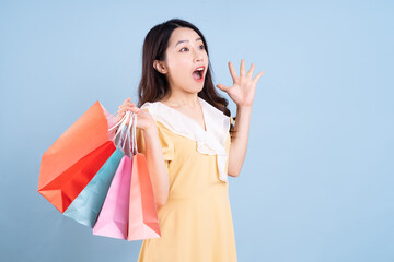 Beautiful young Asian woman holding shopping bag on blue background