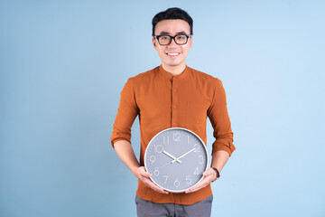 Young Asian man holding clock on blue background