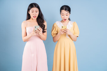 Two young Asian women wearing dress on blue background