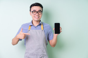 Young Asian man wearing apron posing on green background