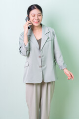 Young Asian businesswoman holding smartphone on green background