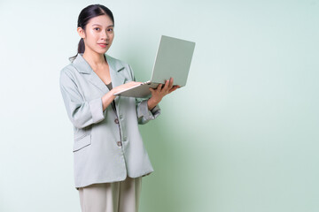 Young Asian businesswoman holding laptop on green background