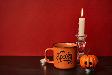 Cup with drink next to burning candles and halloween pumpkin on bloody background