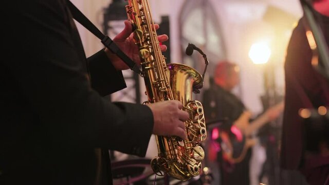 Musical band group playing song, performing on concert musician stage with lights. Saxophone player playing a solo in jazz band, performing on lightened stage. Sax musician player with band at concert