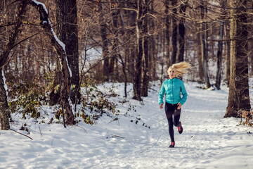 Fit sportswoman jogging on snowy path in forest at winter. Healthy lifestyle, winter fitness