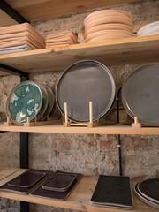 Handmade empty clay dishes composition on a wooden shelfs in a shop and with bricks in background