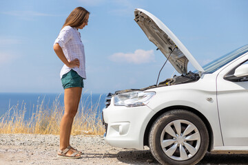 Young slim puzzled woman standing near her rented car during summer vacation