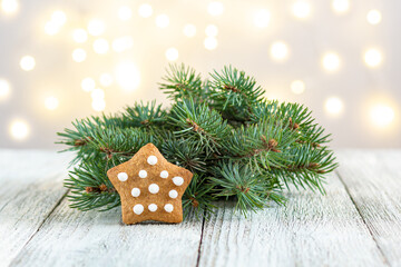 Fototapeta na wymiar Gingerbread star with fir tree branch on bokeh lights background