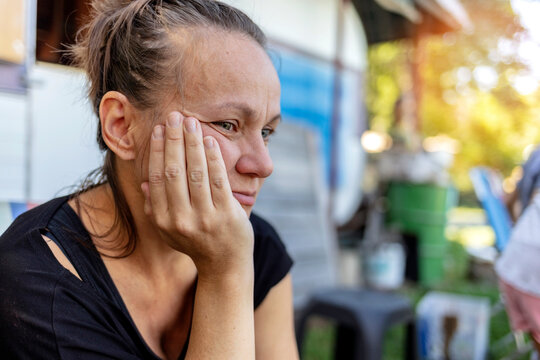 Shot of sad woman sitting outdoor. Woman outdoors in nature holding her head expressing pain, exhaustion, sadness or depression. Concerned serious mature woman. Photo of a beautiful thoughtful female.