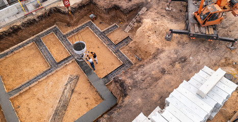 Construction site with workers pouring concrete in formwork with reinforcement. Wet cement pours to civil building foundation, aerial view.