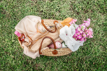 Picnic basket with wine, baguette, wine glass, flowers, candle and picnic blanket on green grass...