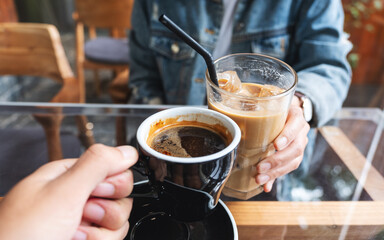 Closeup of a woman and a man clinking coffee cups together in cafe