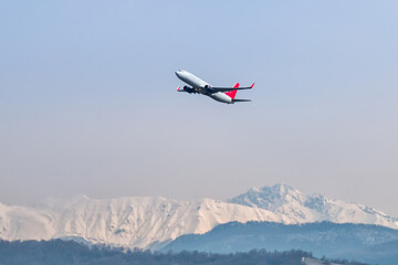 Fototapeta na wymiar Takeoff of a passenger airliner against the backdrop of high mountains covered with snow