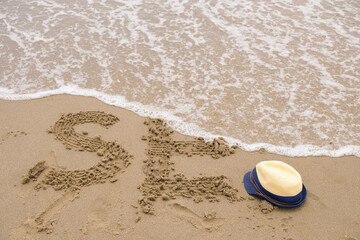 Fototapeta na wymiar Sea waves washing away the letters on the sand. Children's sun hat and remnants of the word Sea.