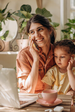Smiling businesswoman young woman with her little daughter is using a laptop at home office.Mom is on the phone.Remote work at home, freelance, working moms,online education.Selective focus.