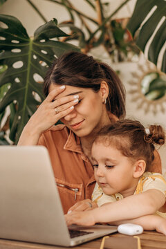 Tired Businesswoman Young Woman Of Mixed Race With Her Little Daughter Is Using A Laptop At Home Office.Child Distracts Mom From Work.Remote Work At Home, Freelance, Working Moms,online Education.