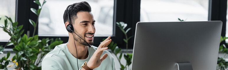 Smiling muslim businessman in headset having video call on computer in office, banner
