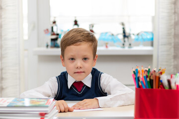 A cute first-grader boy in a school uniform at home while isolated at his desk makes a paper airplane during recess. Selective focus. Portrait
