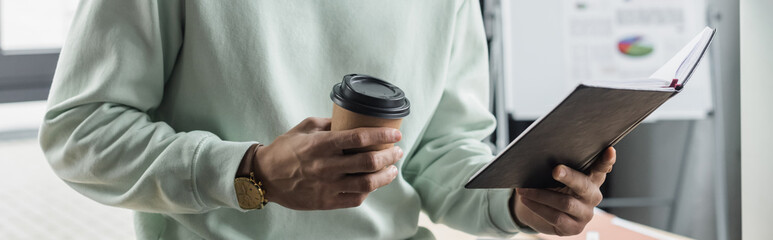 Cropped view of businessman in casual clothes holding notebook and coffee to go in office, banner