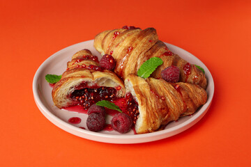 Plate with croissants with raspberry jam on orange background