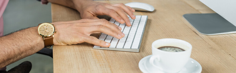 Cropped view of businessman using computer near cup of coffee in office, banner