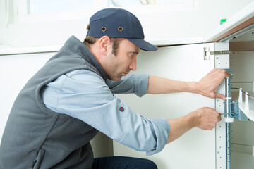 man installing wooden dowels into a particle board shelf