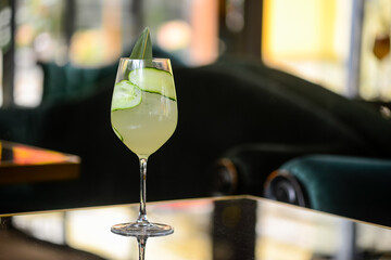 cocktail with cucumber in a large glass on a glass table
