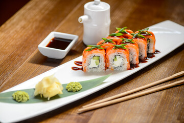Philadelphia sushi roll on a white long plate on a table with sauce and chopsticks
