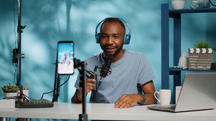 Vlogger using smartphone to record video for vlog channel with microphone, laptop and headphones. Blogger filming with mobile phone for social media content in studio. Man vlogging