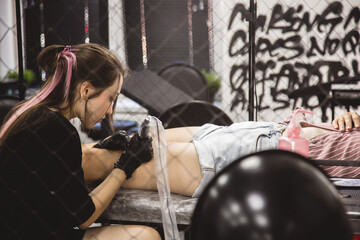 Woman tattoo artist doing tattoo in studio, making tattoo on body. closeup