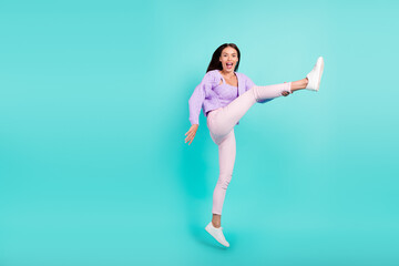 Fototapeta na wymiar Photo of crazy excited lady jump raise leg wear violet cardigan pants sneakers isolated teal color background