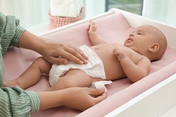 Mother changing her baby's diaper on table at home - obrazy, fototapety, plakaty